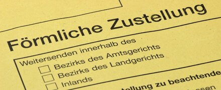 Ein gelber Briefumschlag, der eine förmliche Zustellung signalisiert, liegt auf einem Schreibtisch.